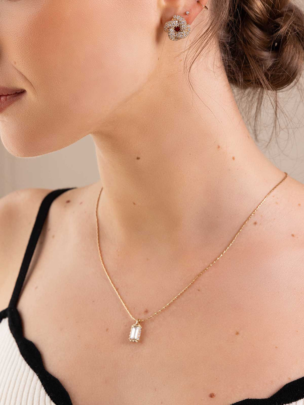 Close-up of a woman wearing a gold necklace and earrings against a neutral background